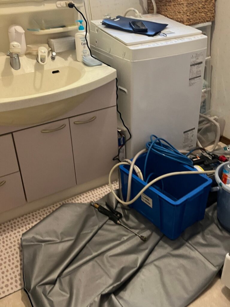 脱衣所の床に広げた保護シートと、青いバケツ、高圧洗浄のホース